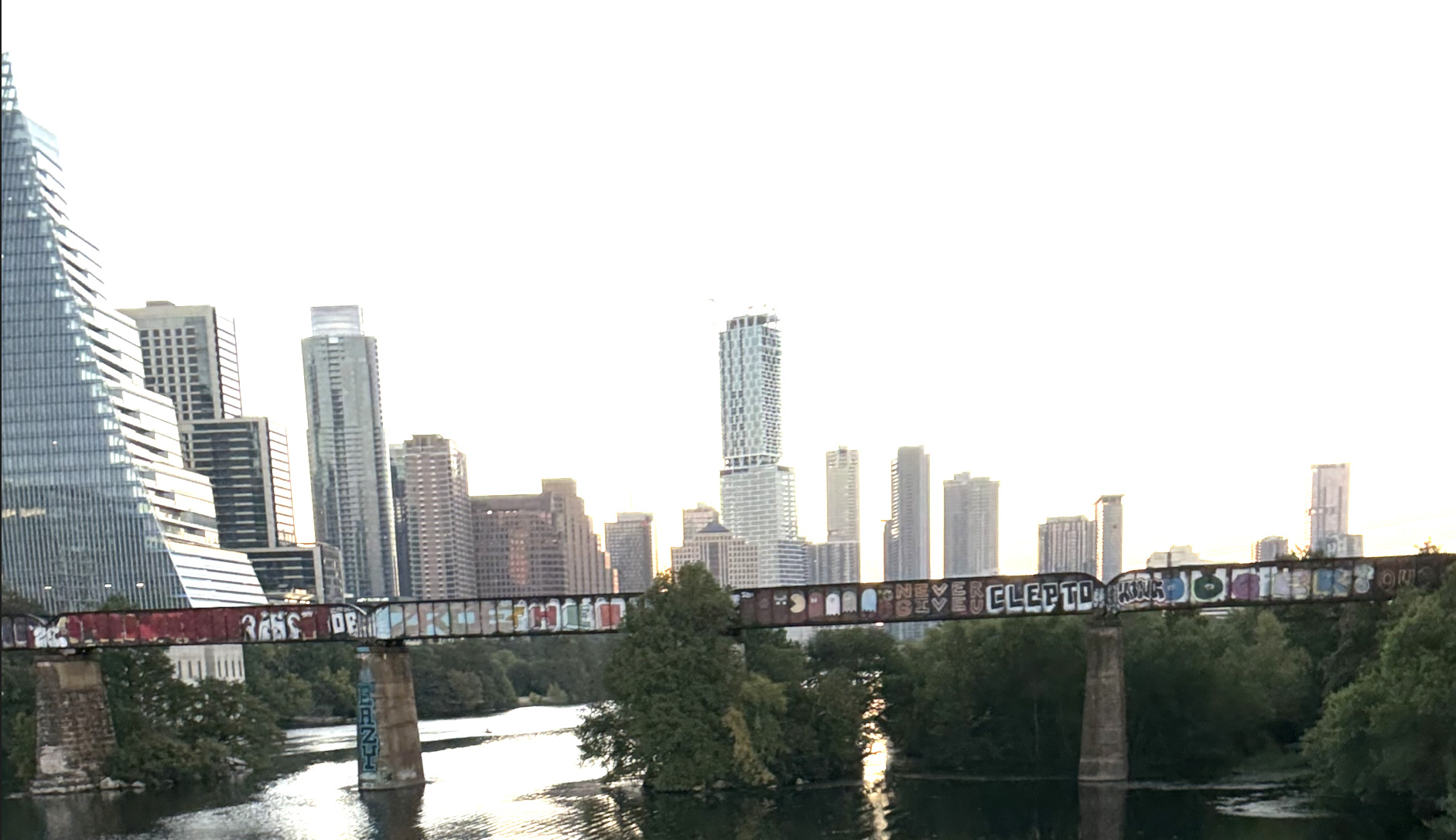 Austin skyline reflected in river, vibrant bridge graffiti.
