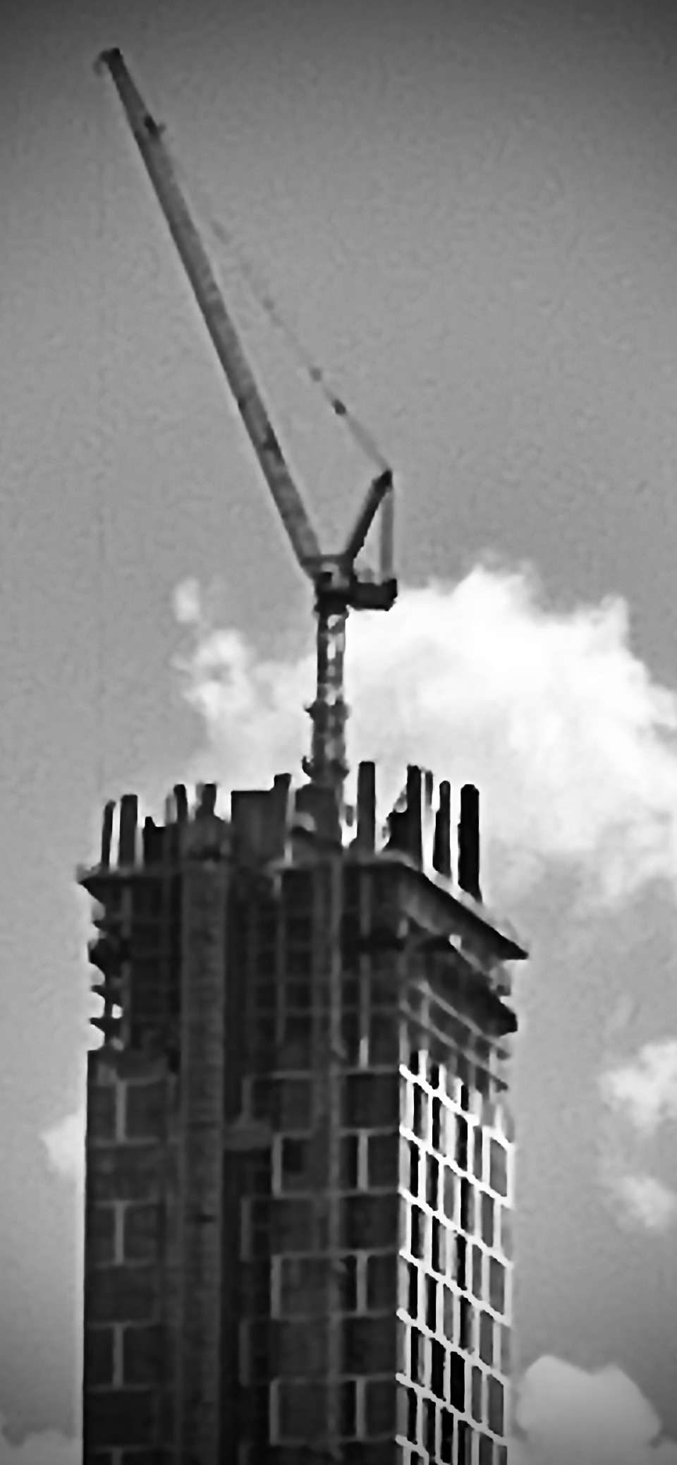 Construction crane looms over a partially-built, grid-like skyscraper.