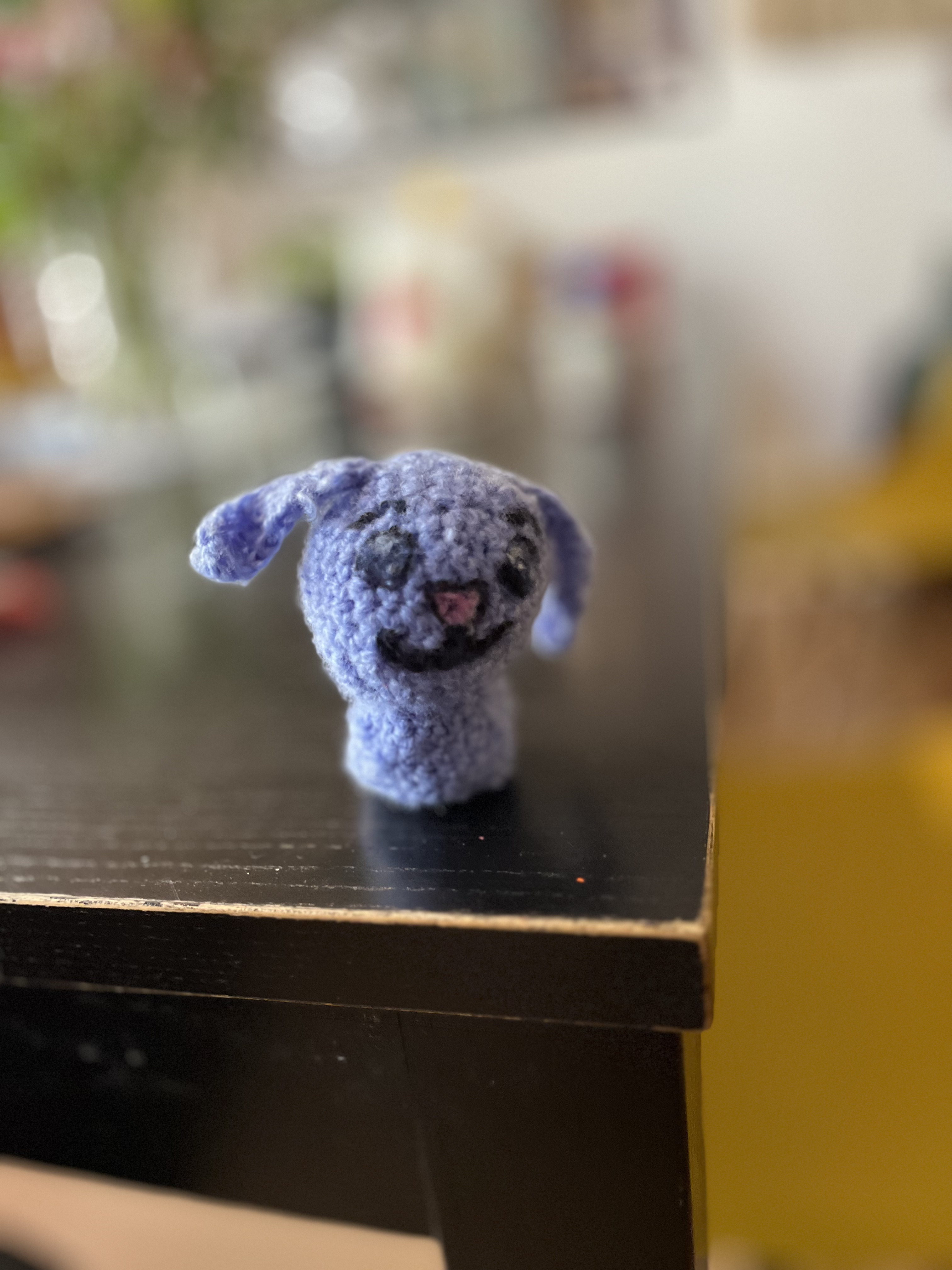 The crocheted friend sits patiently on the black table.